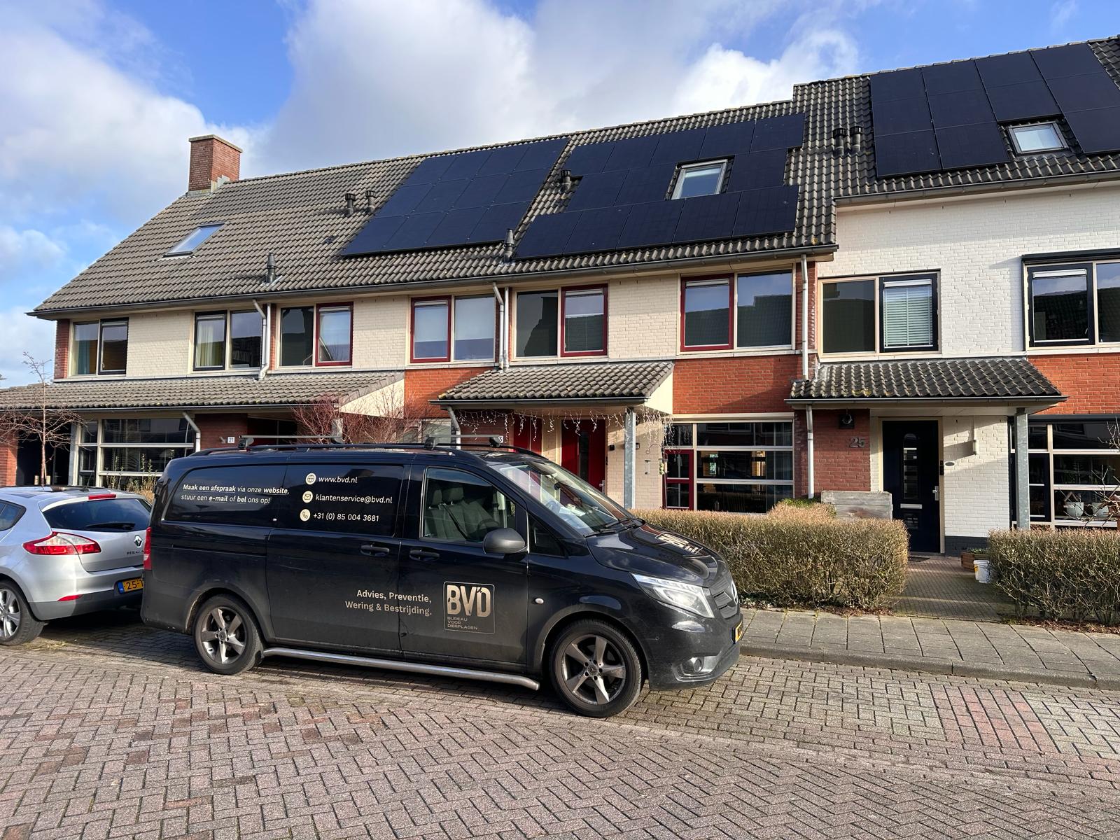 Bedrijfsbus geparkeerd voor een rijtjeshuis met zonnepanelen op het dak.